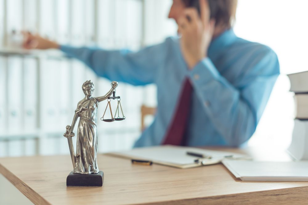 Attorney talking on mobile device in law office, selective focus on statue of Lady Justice