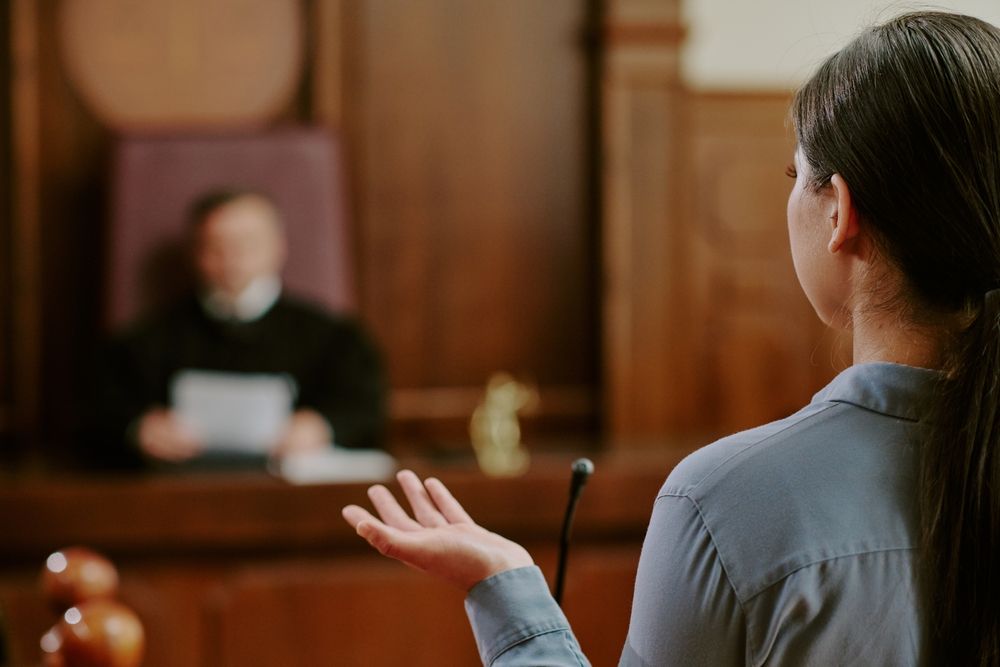 A woman addresses a judge in a courtroom, presenting her case