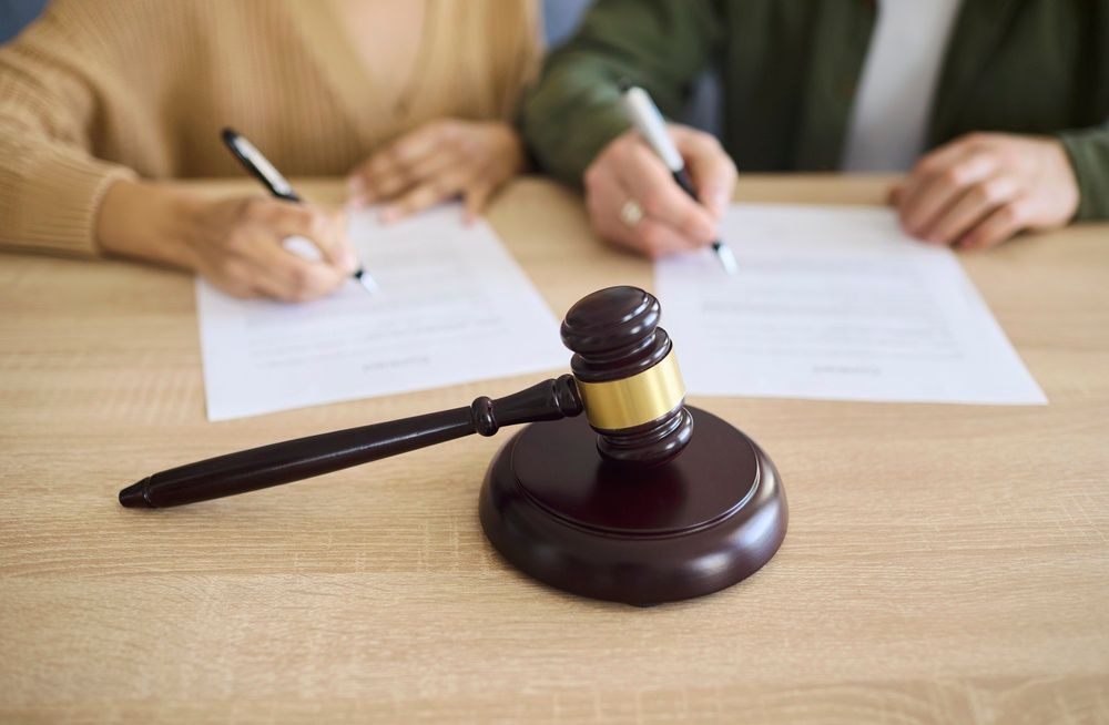 Couple signing divorce document at court with gavel. Focus on legal paperwork and signature for separation agreement, showing mediation, law and asset split. Strong concept of legal conflict.