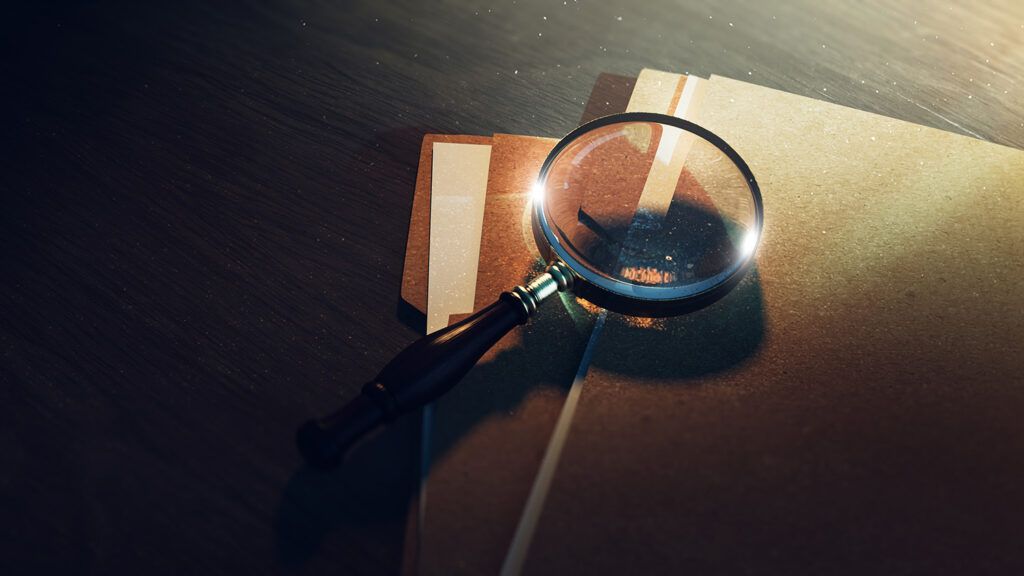 Magnifying glass lying on a couple of manila document folders on a table against a dark background