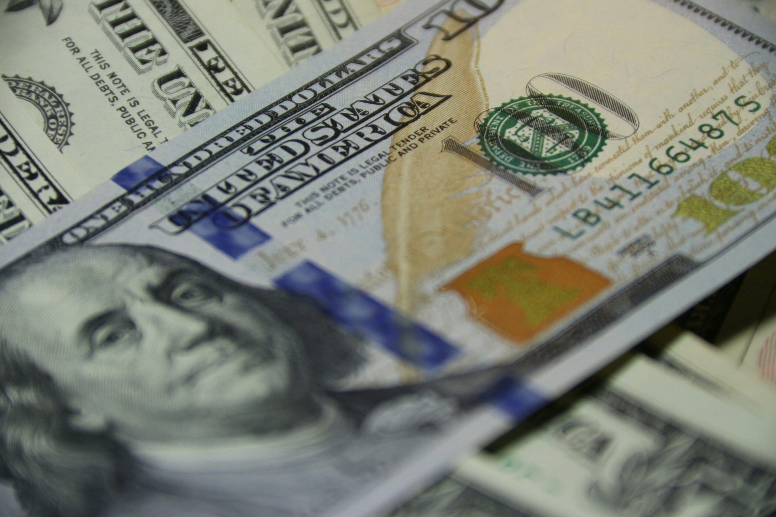 a pile of American dollars with a hundred dollar bill on top