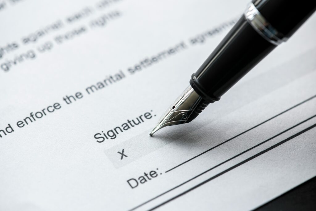 A black fountain pen poised at the signature box on a marital settlement agreement.