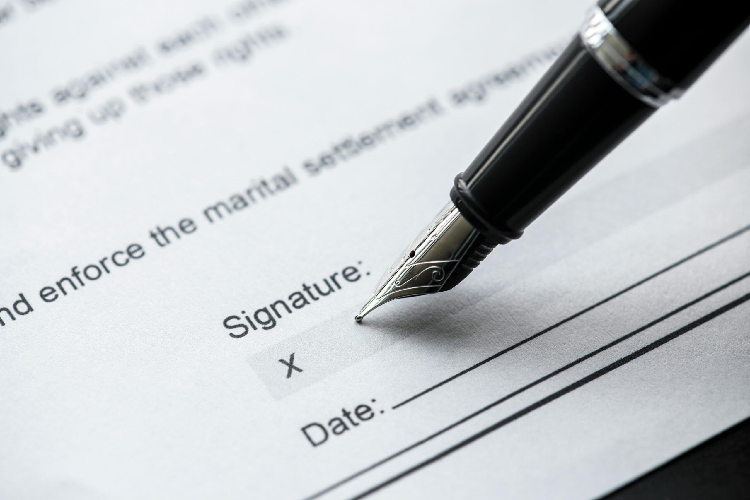 A black fountain pen poised at the signature box on a marital settlement agreement.