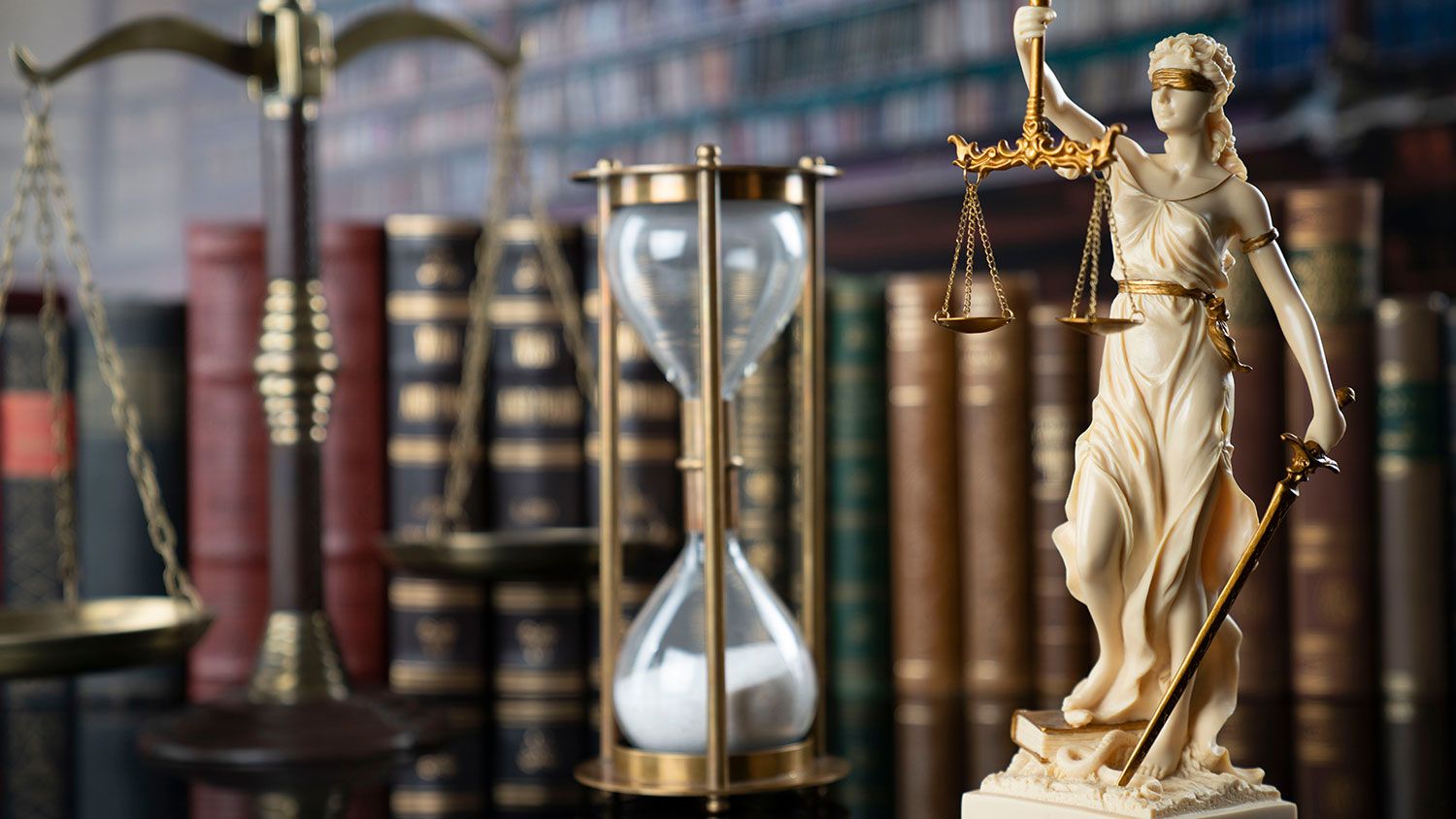 An hour glass surrounded by law books and a "Justice is Blind" statue.