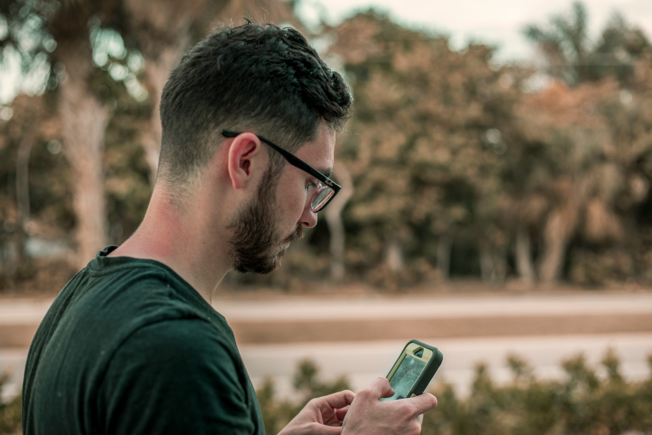A man wearing glasses is focused on his phone, appearing engaged in a conversation or browsing content.