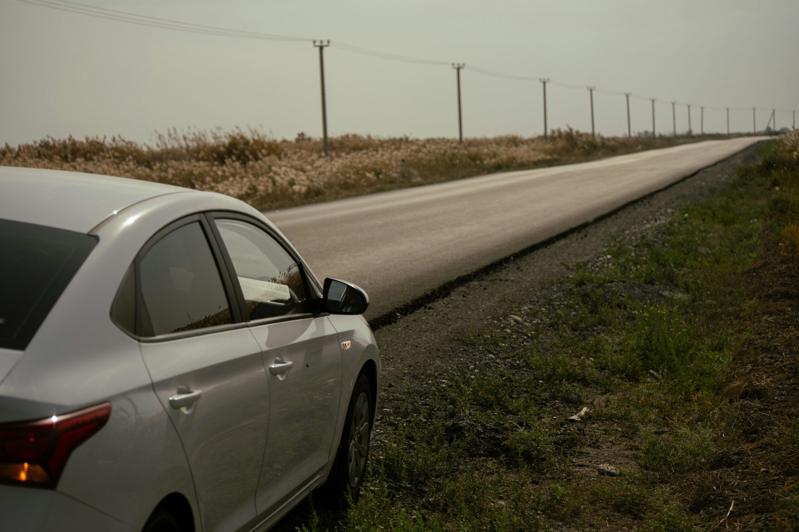 A car is parked on the side of a road, surrounded by grass and trees in a suburban area.