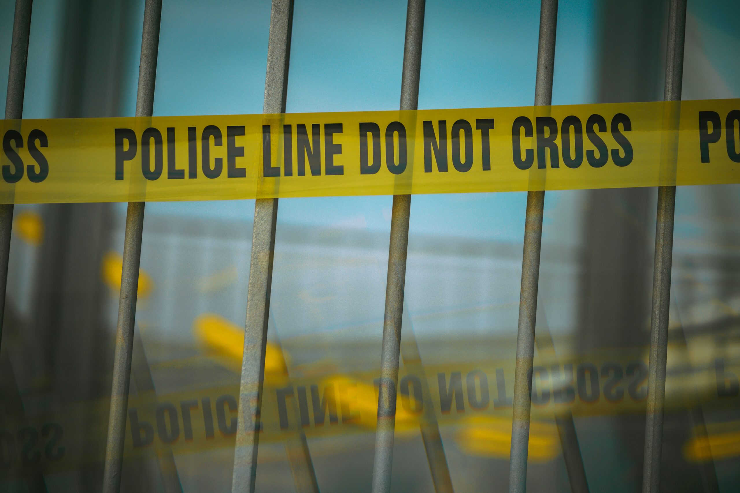 a yellow banner reading "police line do not cross" is wrapped across a metal fence.