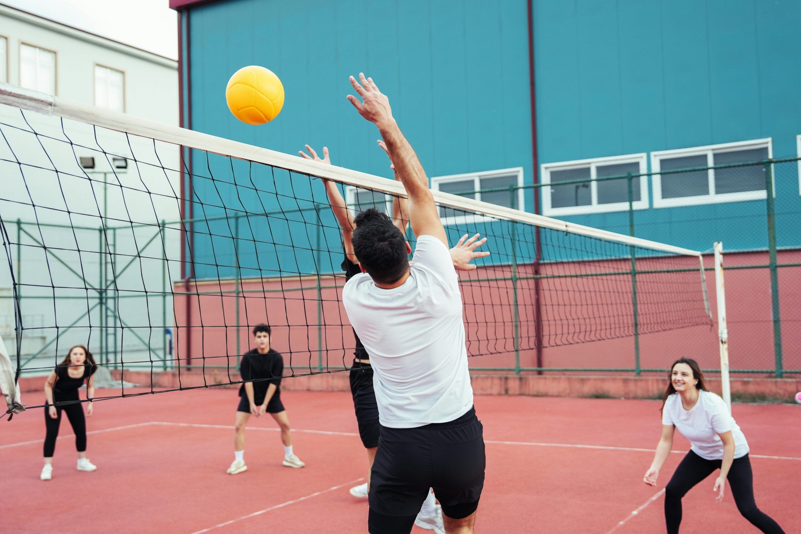 A group of people playing volleyball, with a net in the center and a clear blue sky above.