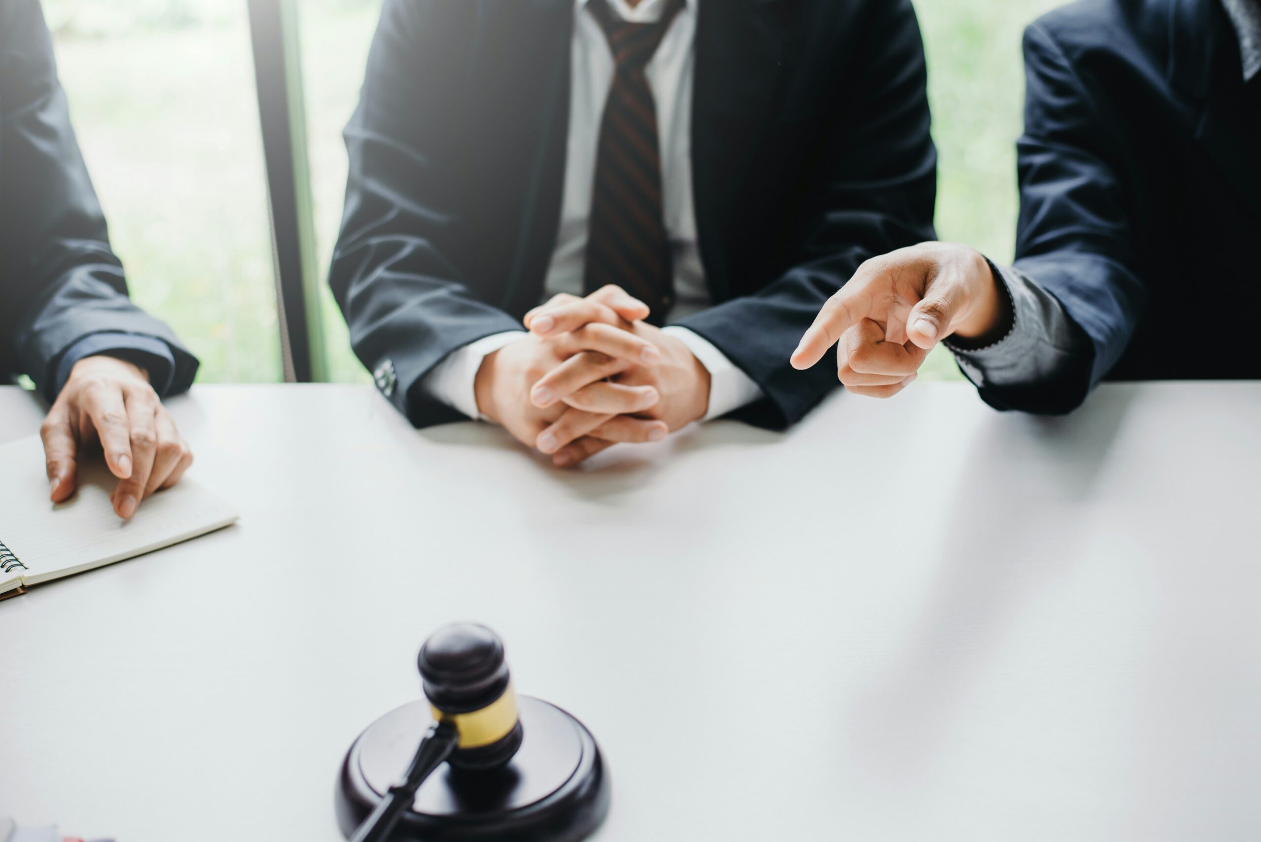 Three men at a table. They are in suits. The one on the right from our POV is pointing. There is a gavel on the table.
