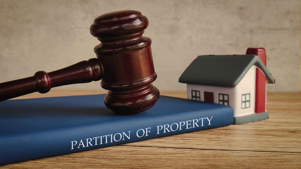 Gavel and a miniature house on a book titled "PARTITION OF PROPERTY," representing legal property division.