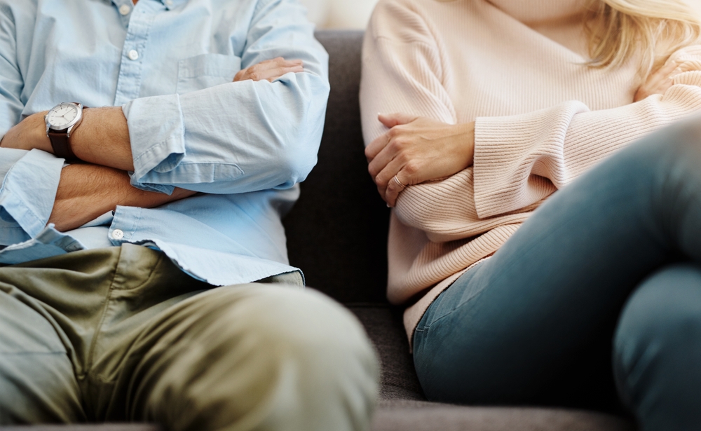 Man and woman sitting apart on a couch with their arms crossed